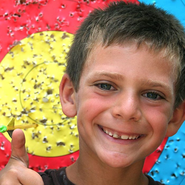 boy camper smiling in front of archery target