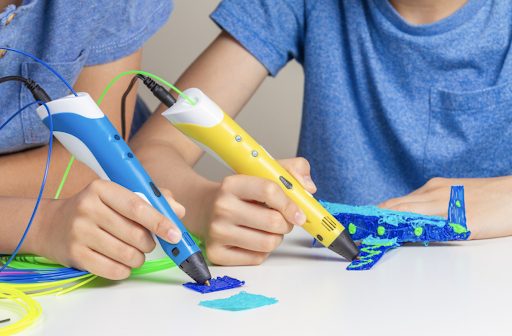 Two kids using 3D printing pens.