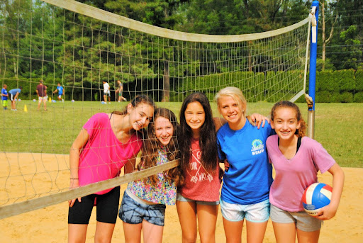 A group of girls smiling on a volleyball court.